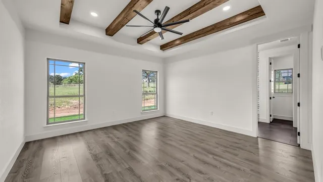 an empty room with wooden floor a ceiling fan and windows