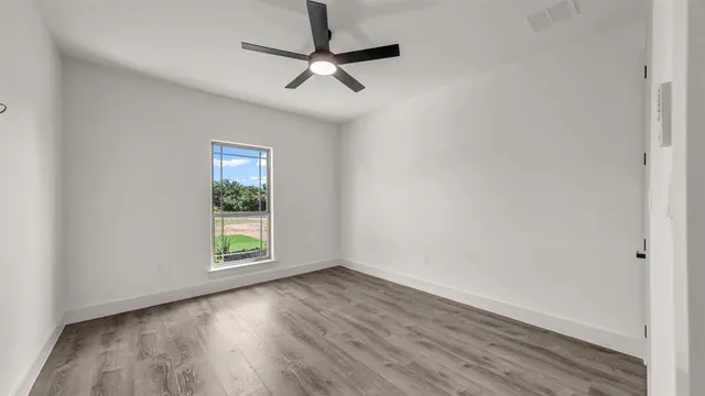 an empty room with wooden floor fan and windows
