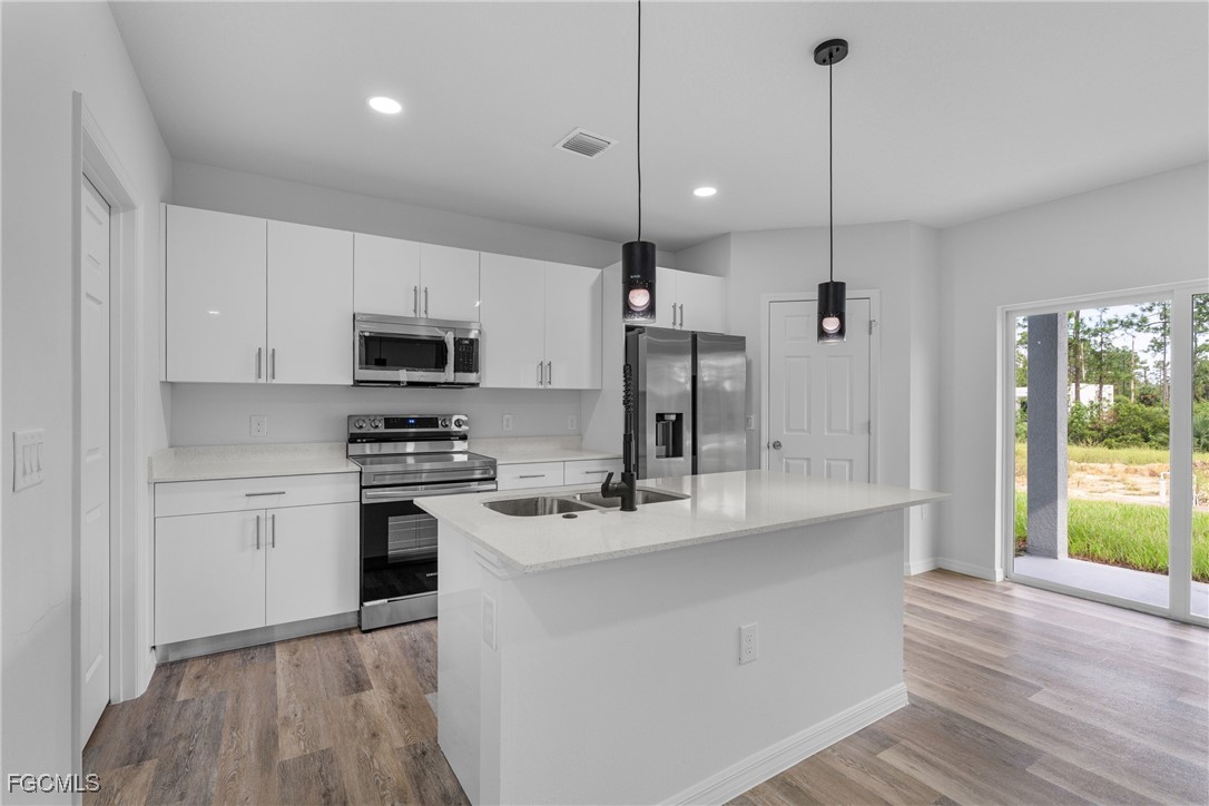 945 Butler Street East Lehigh Acres, FL 33974 - Photo 13 of 34 a kitchen with stainless steel appliances kitchen island a white cabinets and a wooden floor