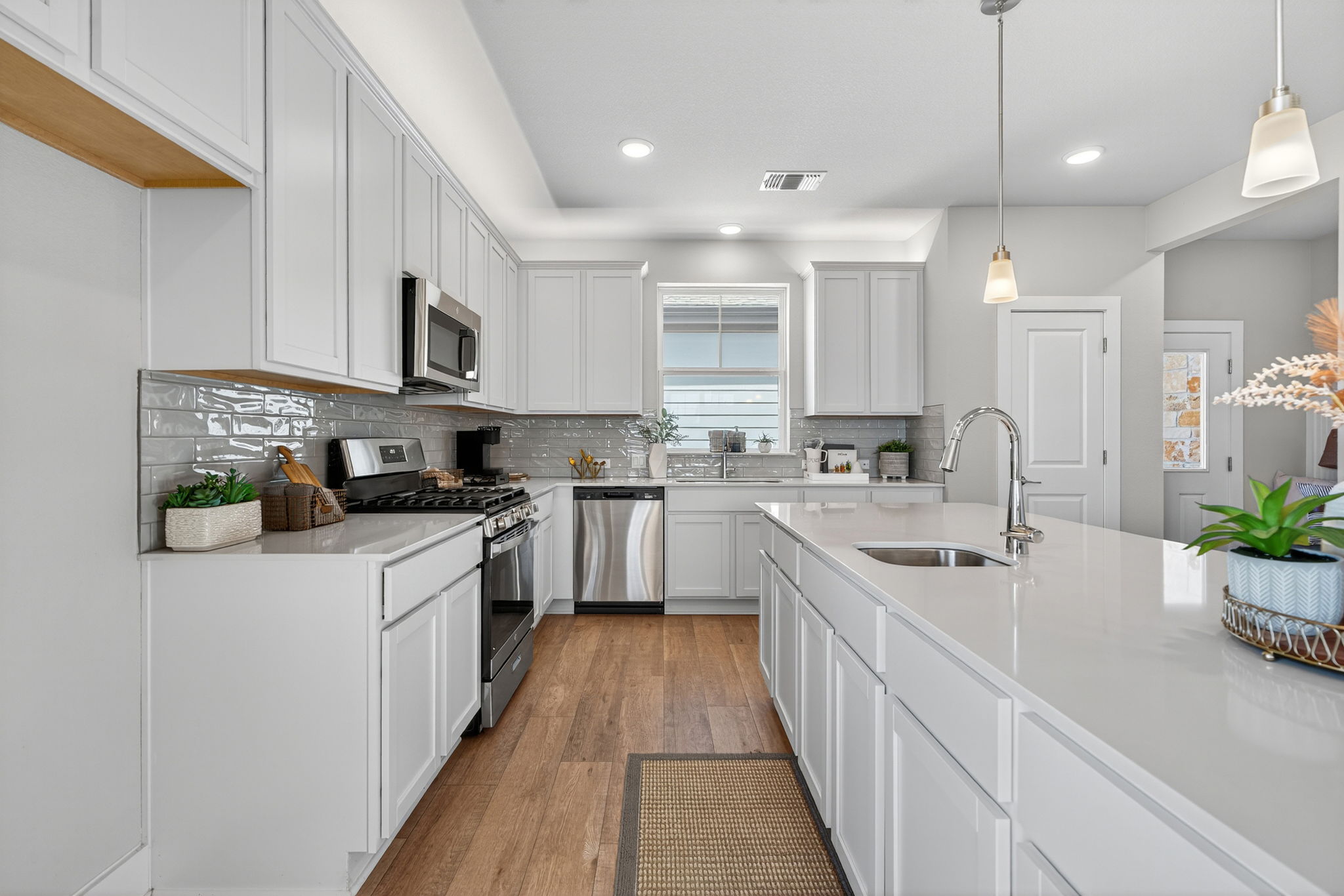 5904 Rotunda View Austin, TX 78747 - Photo 8 of 37 Kitchen featuring stainless steel appliances, light wood-style floors, tasteful backsplash, decorative light fixtures, and white cabinetry