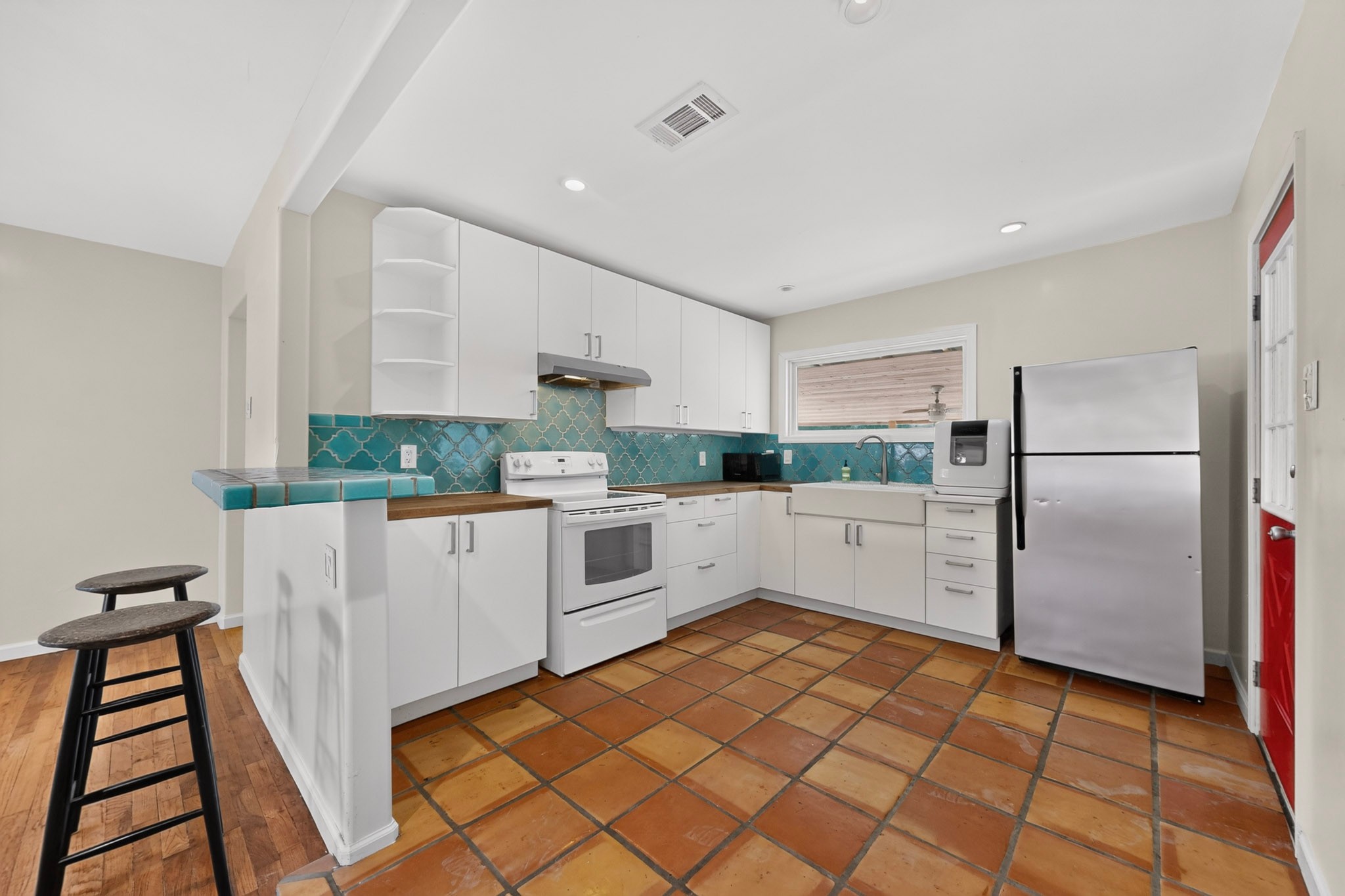 4711 Alf Avenue Austin, TX 78721 - Photo 9 of 34 A well-equipped kitchen features a charming breakfast bar and vibrant backsplash, complementing the classic floor tiles.