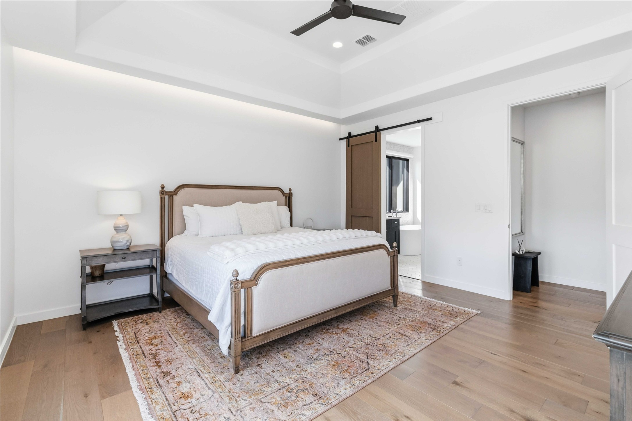 410 Kayak Way Austin, TX 78738 - Photo 18 of 40 Bedroom featuring a raised ceiling, a barn door, light wood-type flooring, a ceiling fan, and recessed lighting