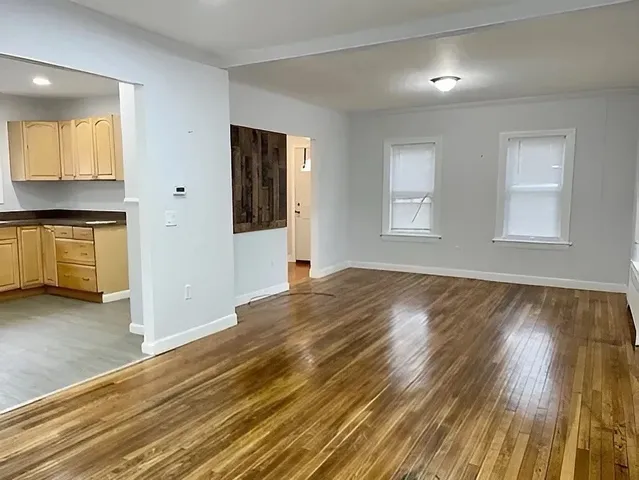 a view of a kitchen and an empty room with wooden floor