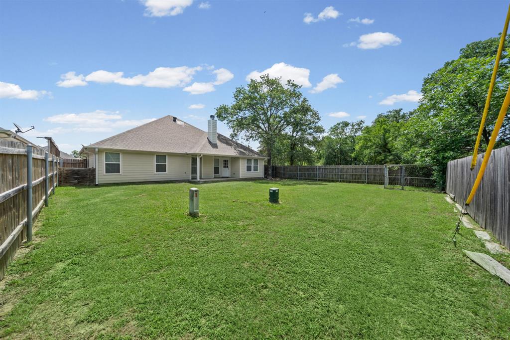 229 Firefly Drive Springtown, TX 76082 - Photo 25 of 33 Expansive backyard featuring a manicured lawn, full perimeter wood fencing, and a tan siding exterior
