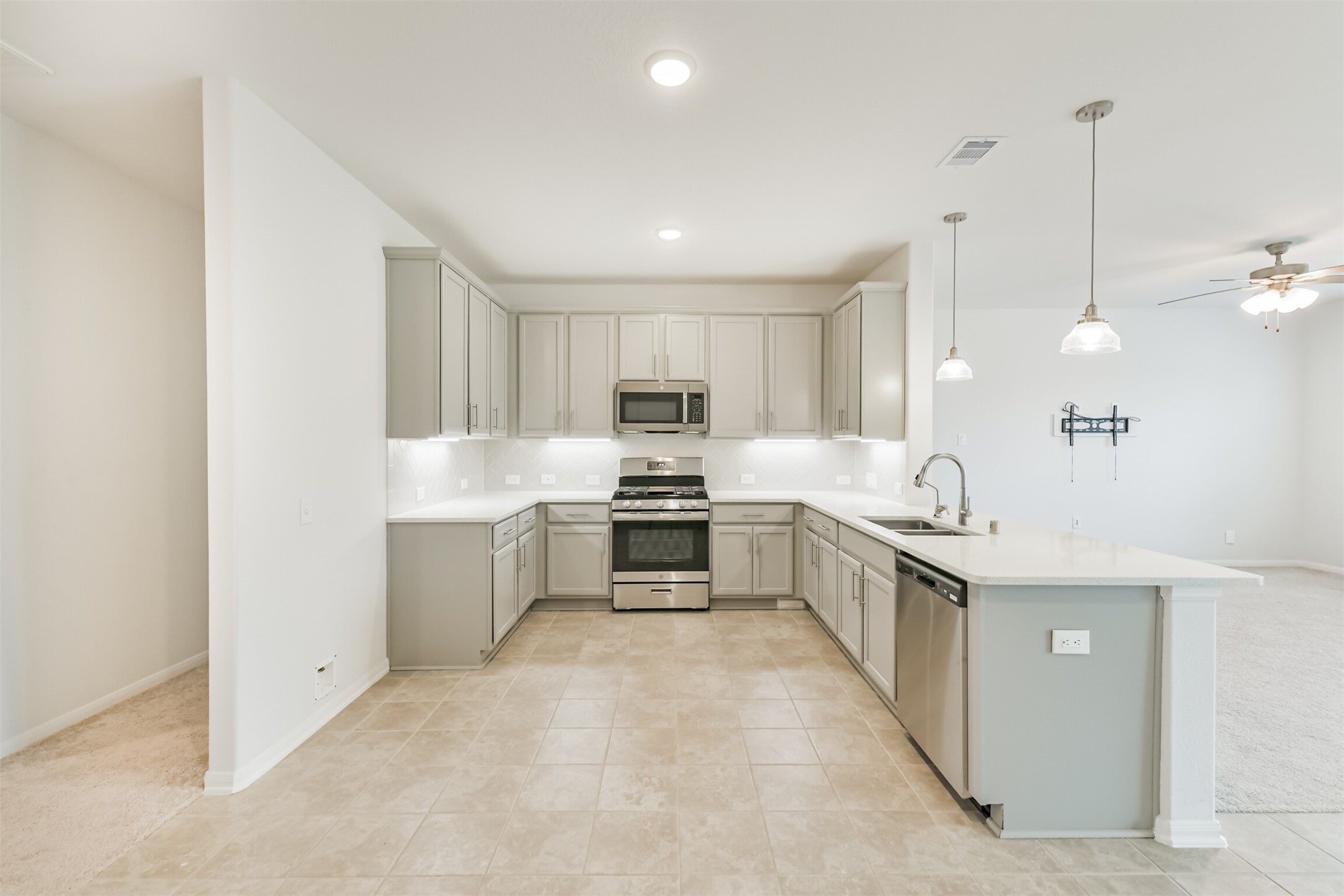 2129 Solstice Boulevard Spring, TX 77386 - Photo 15 of 43 Modern kitchen with stainless steel appliances, gas range, quartz-style counters, under-cabinet lighting, and an abundance of cabinetry for easy storage. The large island with double sinks overlooks the open living area, creating the perfect setup for cooking and entertaining.