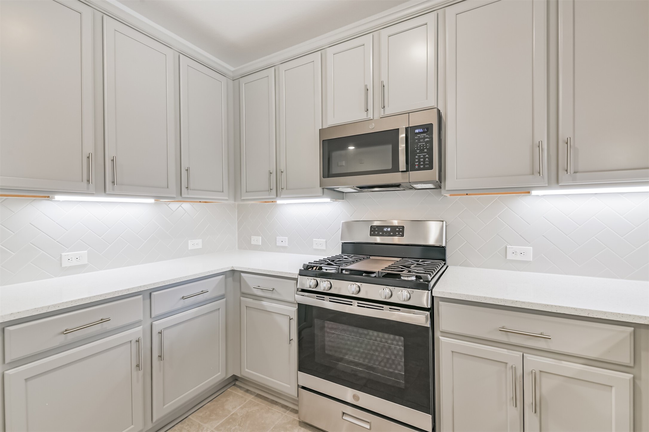 2129 Solstice Boulevard Spring, TX 77386 - Photo 19 of 43 Sleek kitchen with stainless steel gas range and microwave, quartz-style counters, under-cabinet lighting, and abundant cabinetry. The herringbone backsplash adds a modern, upgraded touch to this bright and functional cooking space.