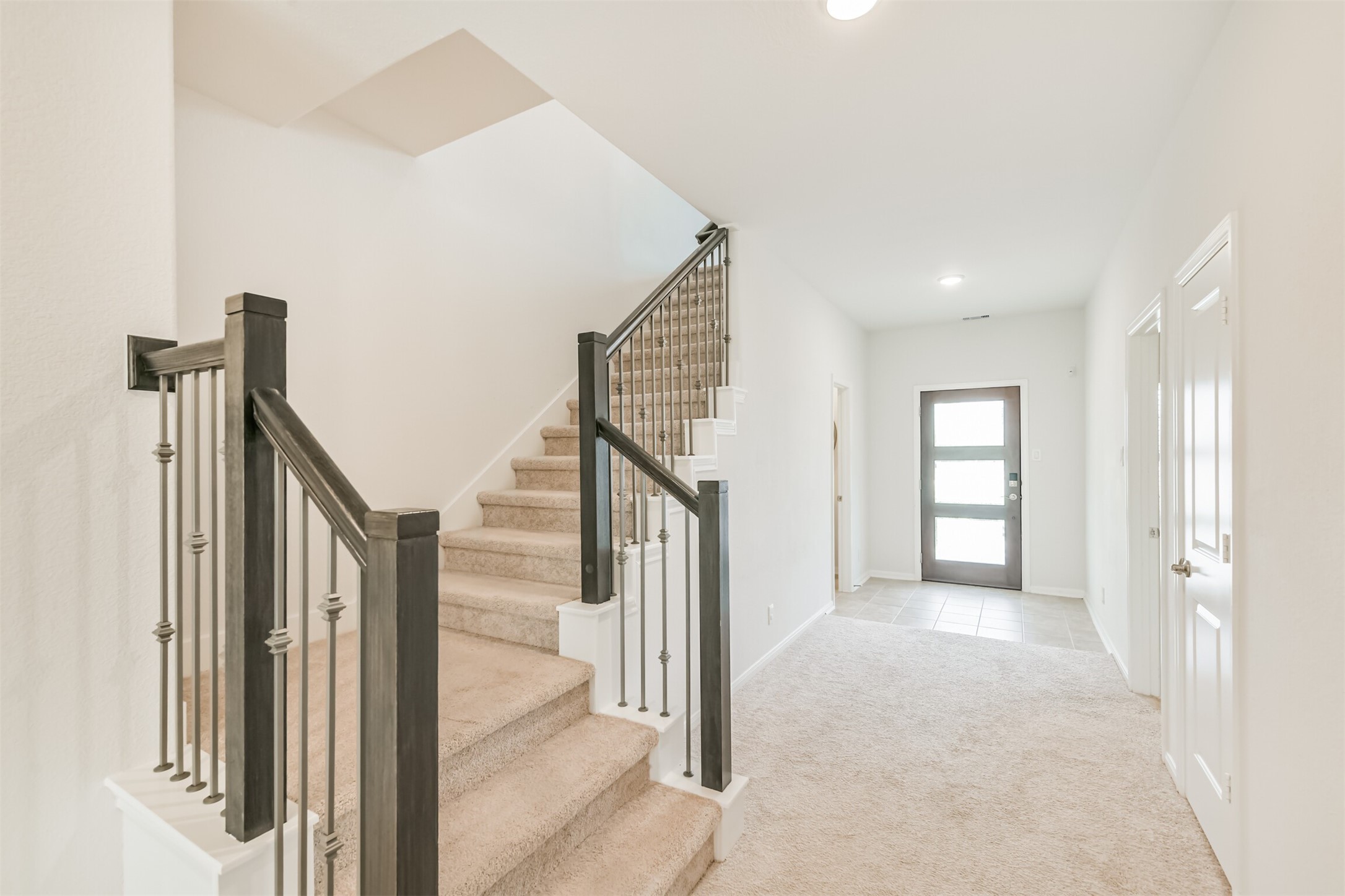 2129 Solstice Boulevard Spring, TX 77386 - Photo 10 of 43 Modern staircase with iron spindles and fresh neutral tones throughout. This open hallway offers easy flow between the front entry, downstairs rooms, and main living areas. Bright natural light from the front door enhances the open, welcoming feel.