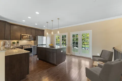 a kitchen with stainless steel appliances granite countertop a refrigerator a sink dishwasher a stove and a dining table with wooden floor