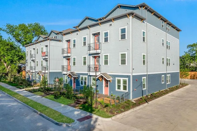 a view of a white building among the street with plants and large trees