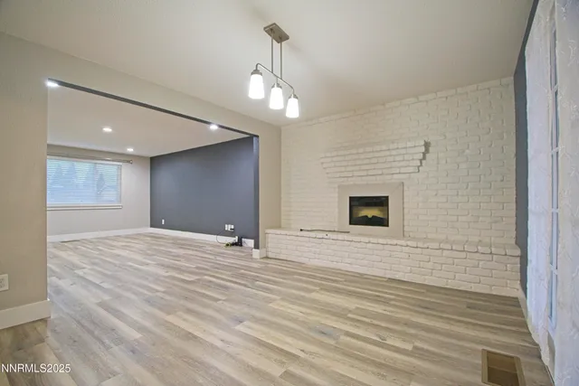 a view of an empty room with wooden floor and a kitchen