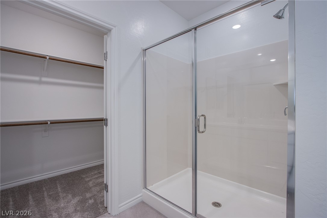 2555 Hampton Road, Unit 11201 Henderson, NV 89052 - Photo 18 of 24 A glass-enclosed shower stands adjacent to a carpeted walk-in closet with built-in shelving.
