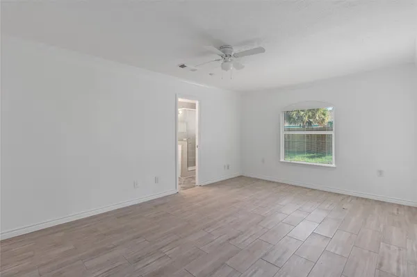 an empty room with wooden floor ceiling fan and windows
