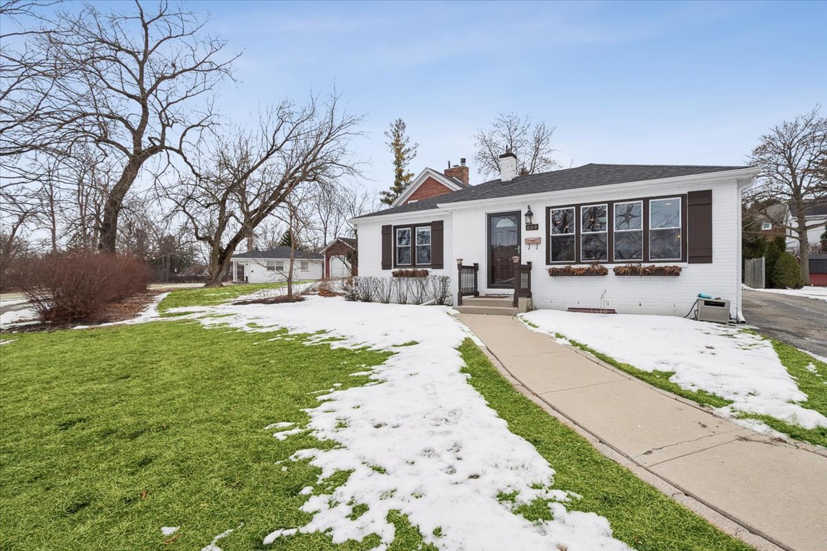 a view of a house with a yard covered with snow and plants