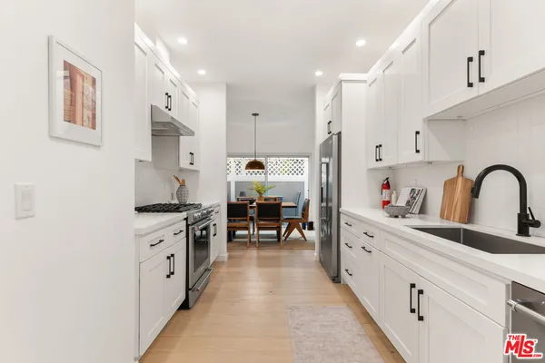 a kitchen with stainless steel appliances granite countertop a stove top oven a sink dishwasher and white cabinets with wooden floor