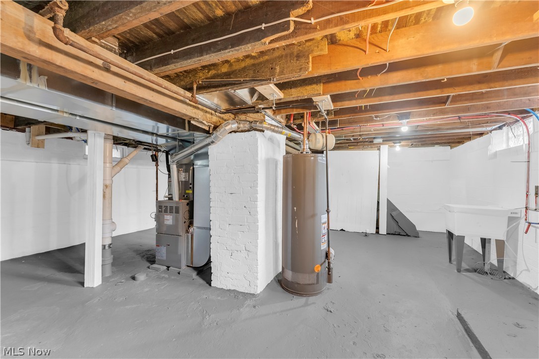 18155 Libby Road Maple Heights, OH 44137 - Photo 28 of 32 Basement space featuring exposed ceiling joists, painted concrete flooring, a utility sink, and a water heater
