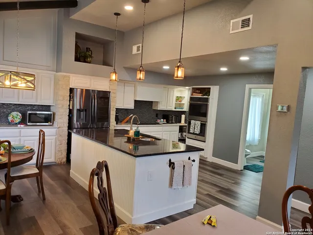 a kitchen with stainless steel appliances kitchen island granite countertop a refrigerator a stove a sink a dining table and chairs with wooden floor
