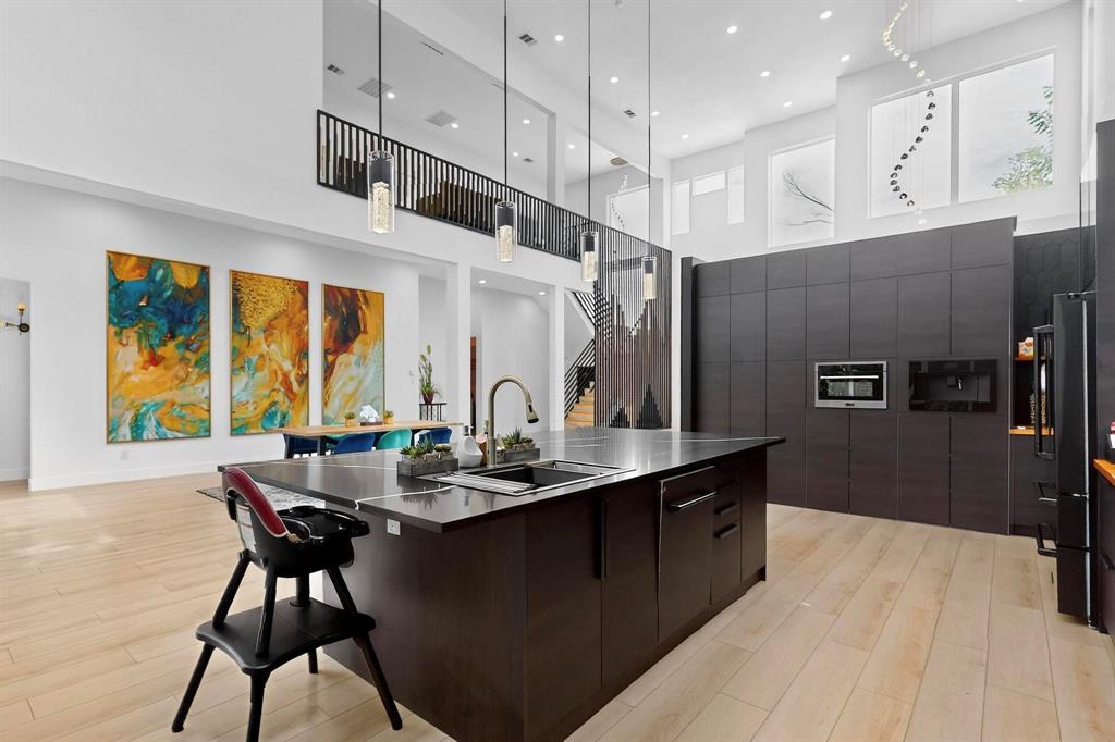 3946 North Cresthaven Road Dallas, TX 75209 - Photo 9 of 38 Modern kitchen featuring a large island with an undermount sink and dark countertop, integrated appliances, light wood-finish flooring, and high ceilings with upper-level windows