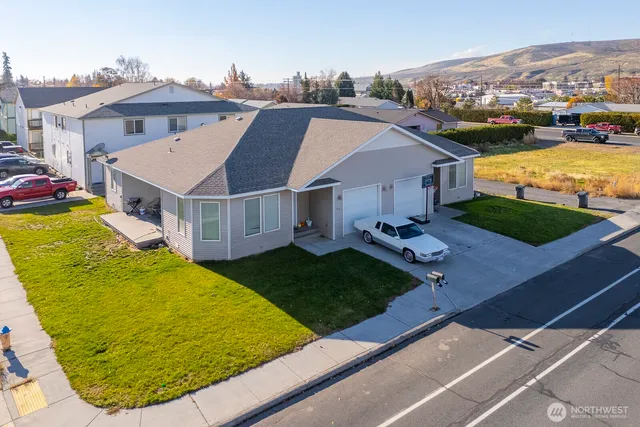 a view of a white building with a big yard plants and large trees