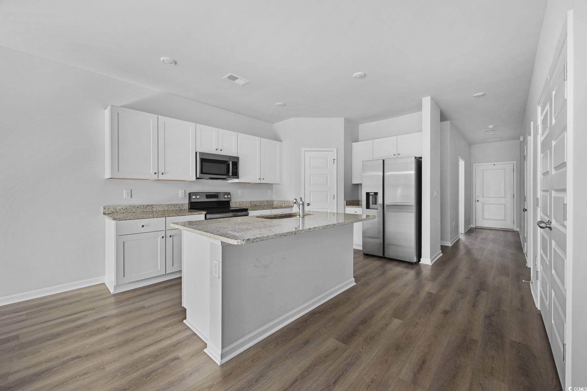 608 Sea Sparrow Street, Unit 608 Myrtle Beach, SC 29588 - Photo 7 of 37 Kitchen featuring white cabinetry, appliances with stainless steel finishes, light stone countertops, a center island with sink, and dark wood-type flooring