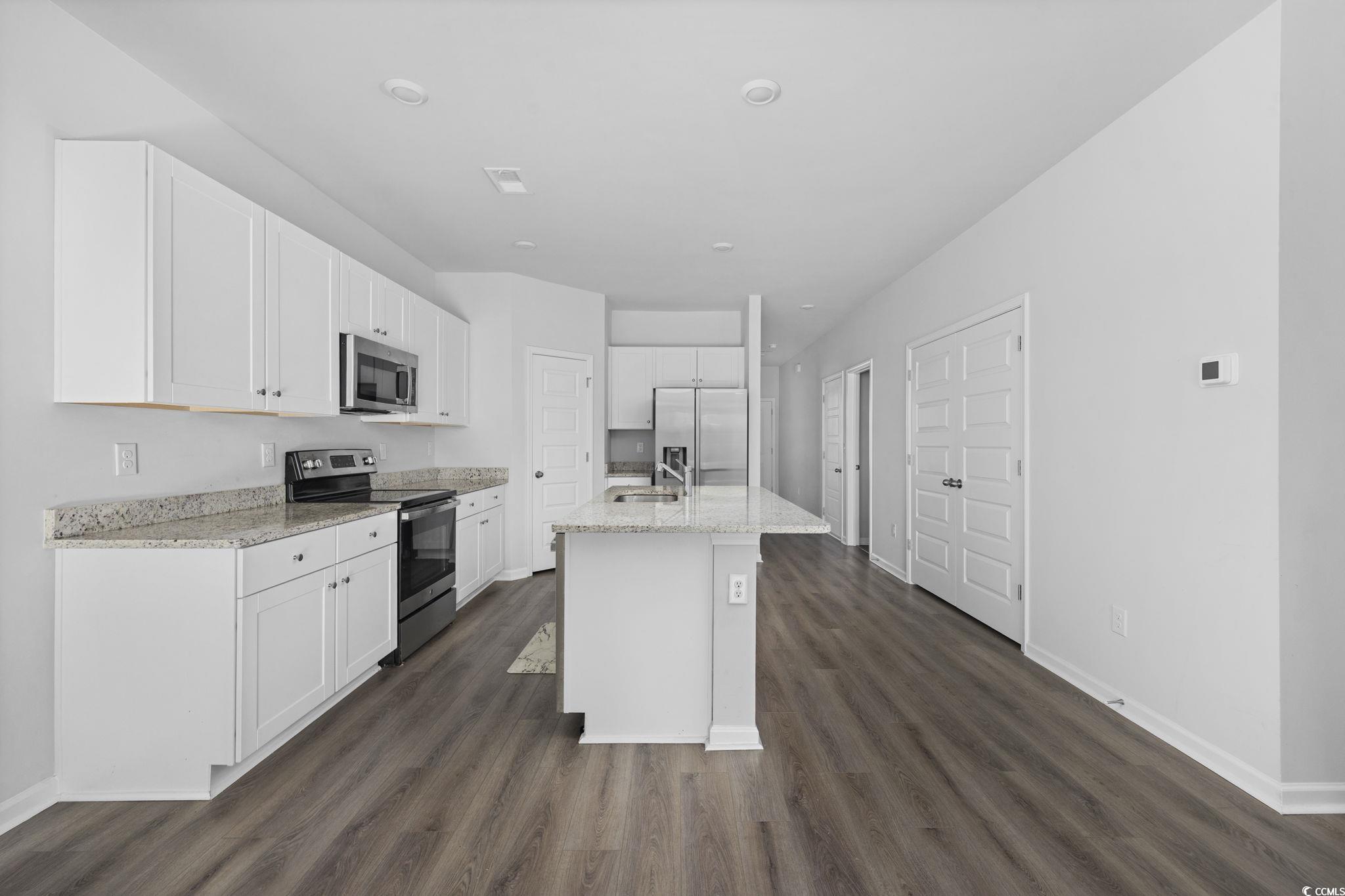 608 Sea Sparrow Street, Unit 608 Myrtle Beach, SC 29588 - Photo 8 of 37 Kitchen with appliances with stainless steel finishes, white cabinets, light stone countertops, a kitchen island with sink, and dark wood-type flooring
