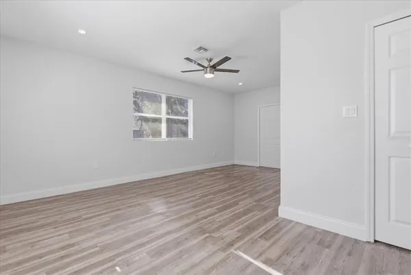 an empty room with wooden floor ceiling fan and windows
