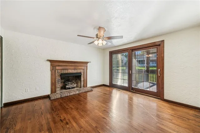an empty room with wooden floor a ceiling fan and fireplace