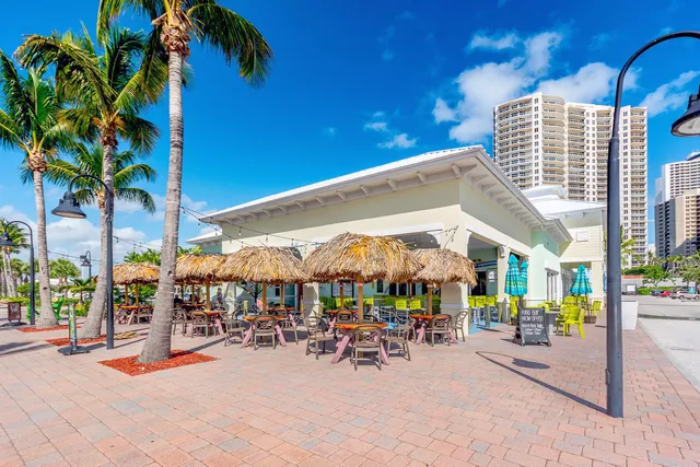 a view of a patio with dining table and chairs under an umbrella with palm trees