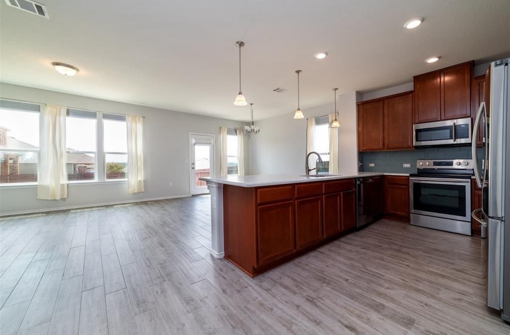 7013 Lickeen Court Austin, TX 78744 - Photo 18 of 20 a kitchen with stainless steel appliances kitchen island granite countertop wooden floors wooden cabinets and sink