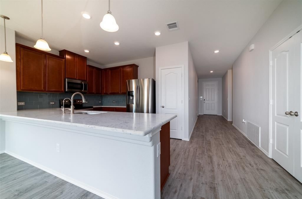 7013 Lickeen Court Austin, TX 78744 - Photo 3 of 20 a view of a kitchen with kitchen island a sink wooden floor and a refrigerator