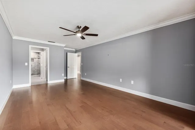 a view of an empty room with wooden floor and a ceiling fan