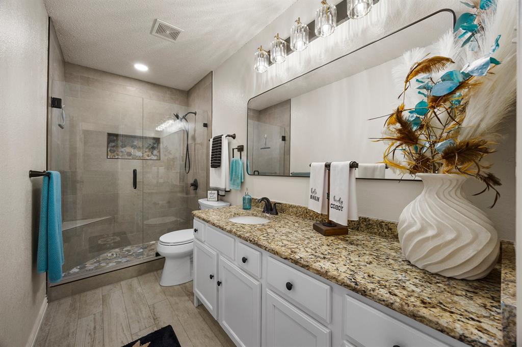7210 Mercurys Road Rowlett, TX 75089 - Photo 15 of 26 a bathroom with a granite countertop sink a toilet and shower