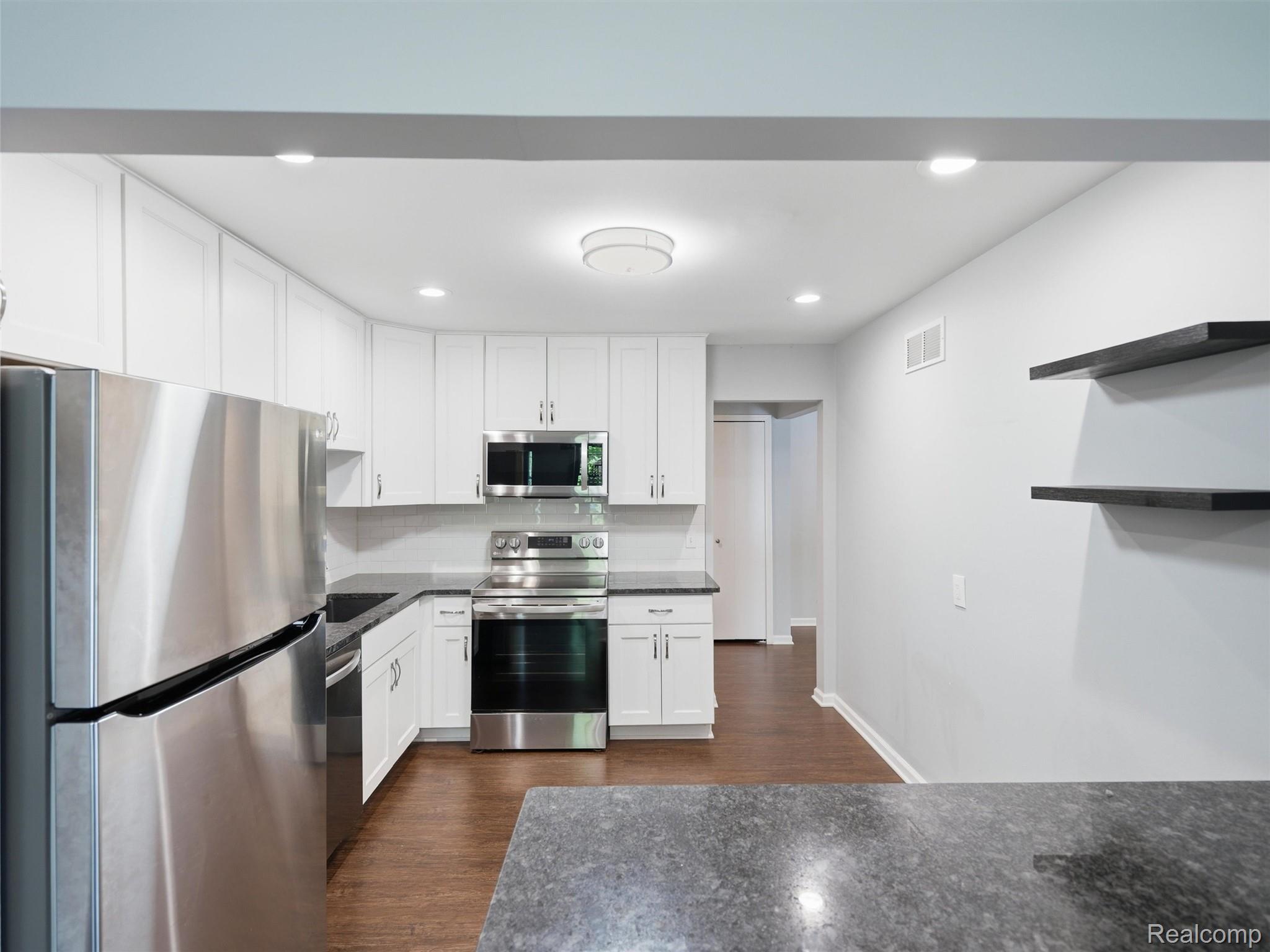 29636 Middlebelt Road, Unit 2602 Farmington, MI 48334 - Photo 14 of 34 Modern kitchen featuring white cabinetry, stainless steel appliances including a gas range and built-in microwave, dark quartz countertops, recessed ceiling lighting, wood-finish flooring, and open shelving