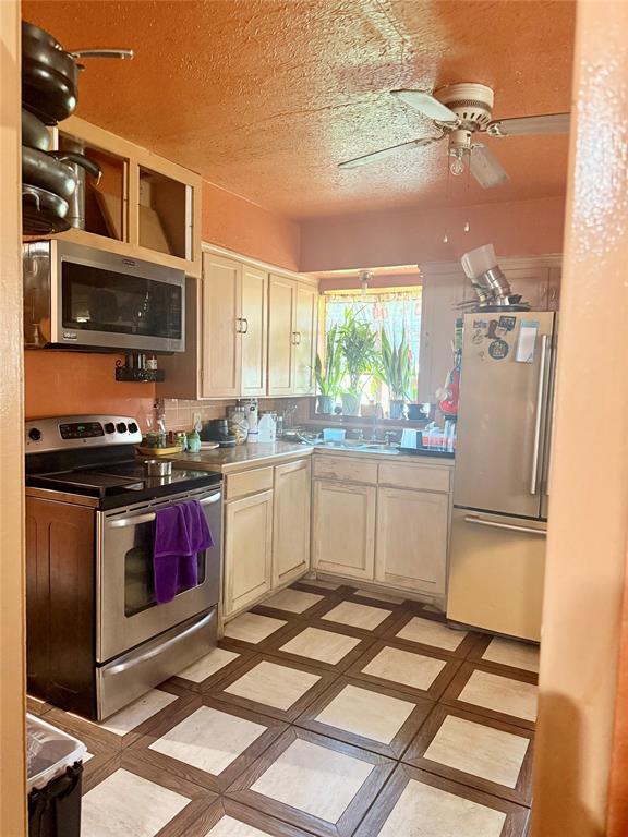 9918 Constance Street Dallas, TX 75220 - Photo 9 of 13 Kitchen with appliances with stainless steel finishes, light countertops, a ceiling fan, light brown cabinetry, and a textured ceiling