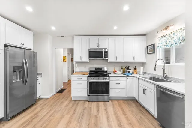 a kitchen with stainless steel appliances white cabinets a sink a stove a refrigerator and a microwave