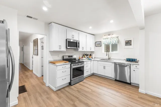 a large kitchen with a stove top oven a sink dishwasher a refrigerator and white cabinets with wooden floor