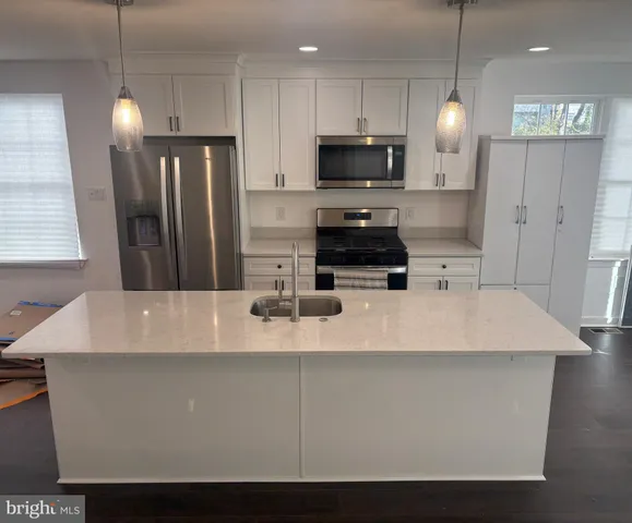 a large kitchen with stainless steel appliances a refrigerator a stove a sink a center island and couches