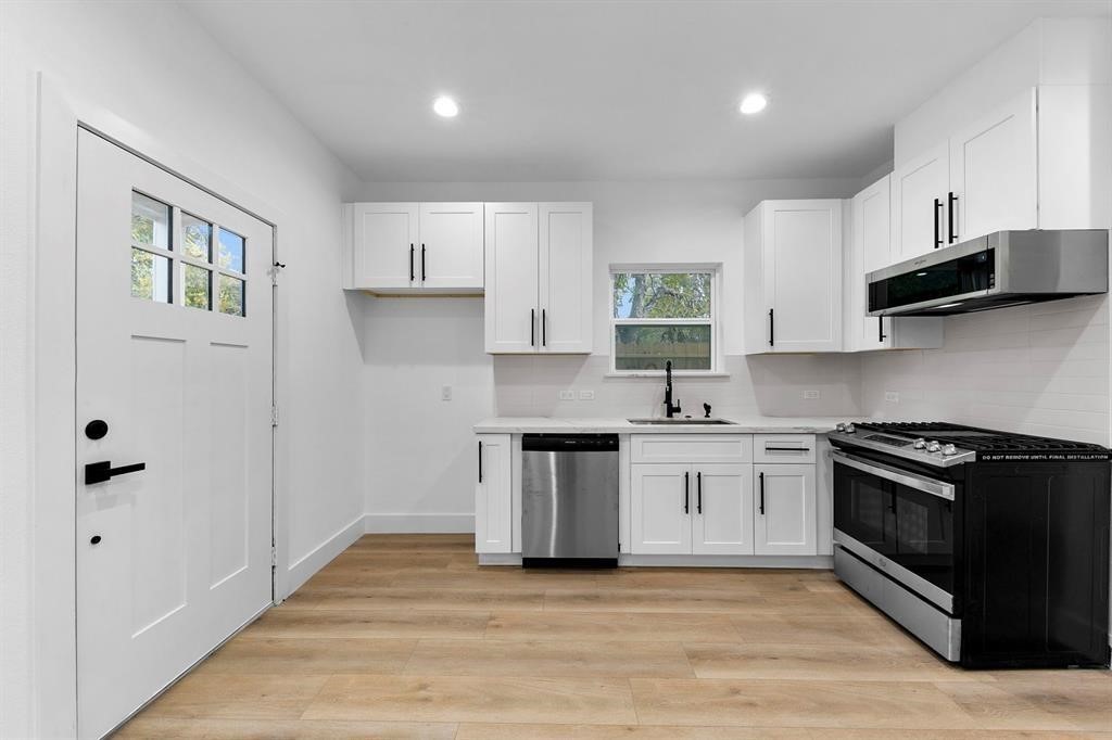 2805 Nettleton Street Houston, TX 77004 - Photo 6 of 9 This modern kitchen features white cabinetry, stainless steel appliances, and light wood flooring. A window above the sink provides natural light, and the space is complemented by recessed lighting.