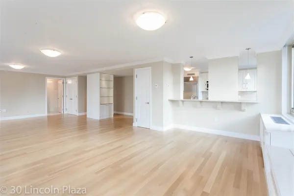 a view of an empty room with wooden floor and a kitchen