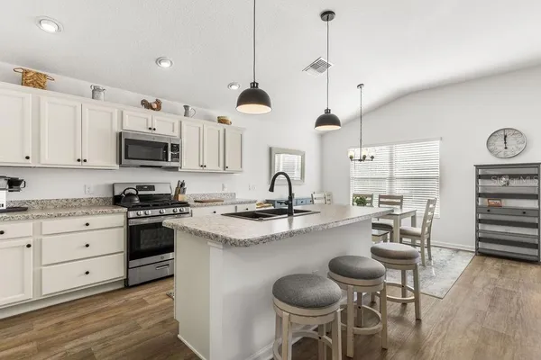 a kitchen with stainless steel appliances kitchen island granite countertop a stove a sink and a refrigerator with wooden floor