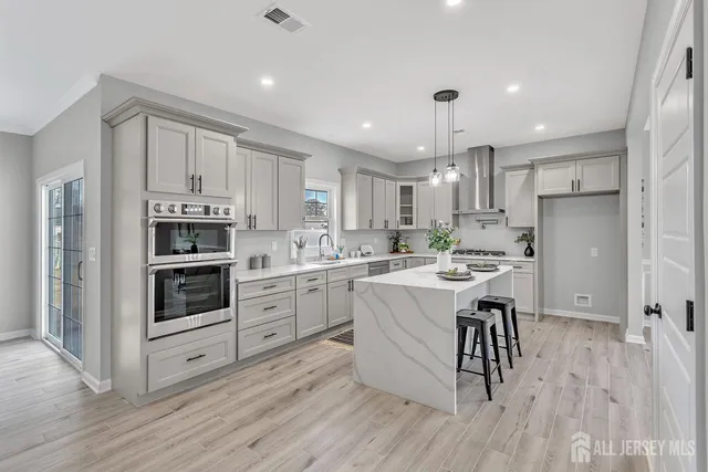 a kitchen with stainless steel appliances kitchen island granite countertop a stove a sink a refrigerator and white cabinets with wooden floor