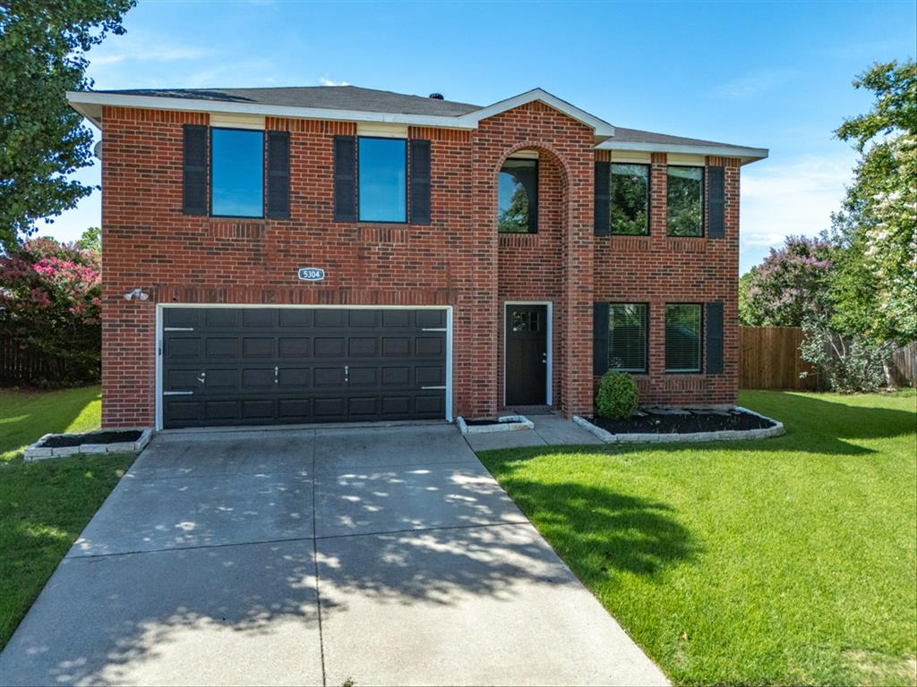 Traditional-style house with driveway, brick siding, and an attached garage