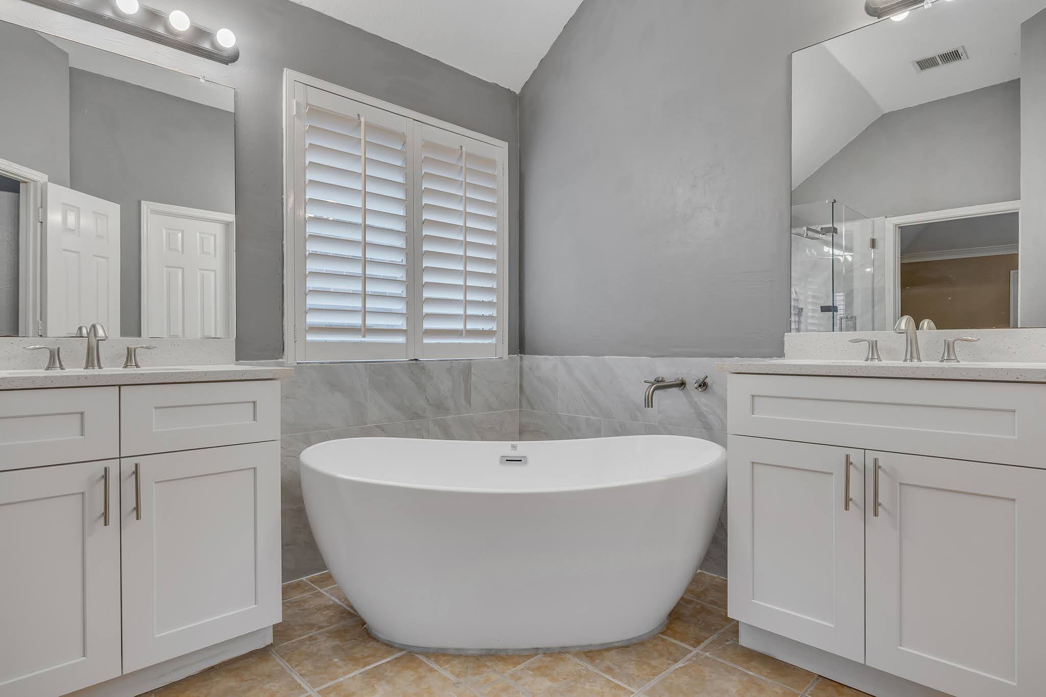 2726 Grimes Ranch Road Austin, TX 78732 - Photo 29 of 35 Full bath with vaulted ceiling, two vanities, tile walls, a freestanding tub, and a wainscoted wall