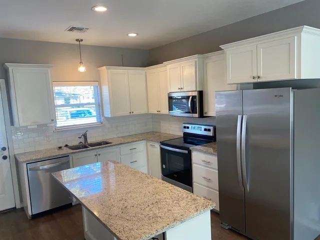 a kitchen with kitchen island granite countertop stainless steel appliances cabinets a sink and a counter space