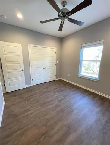 an empty room with wooden floor fan and windows