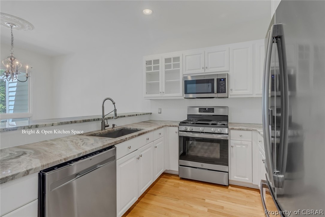 5818 Rivers Landing Terrace, Unit 5818 White Stone, VA 22578 - Photo 17 of 50 Kitchen featuring appliances with stainless steel finishes, light hardwood / wood-style flooring, white cabinetry, sink, and an inviting chandelier