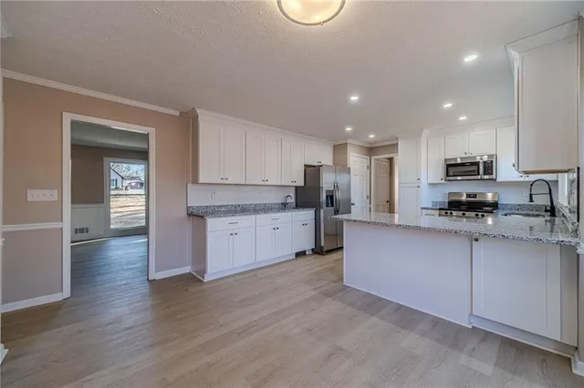 a large kitchen with stainless steel appliances granite countertop a stove a sink a refrigerator and white cabinets with wooden floor