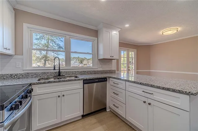 a kitchen with granite countertop stainless steel appliances white cabinets and a large window