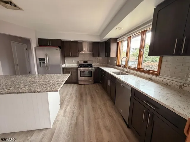 a kitchen with stainless steel appliances granite countertop wooden cabinets a sink dishwasher a stove and a refrigerator with wooden floor