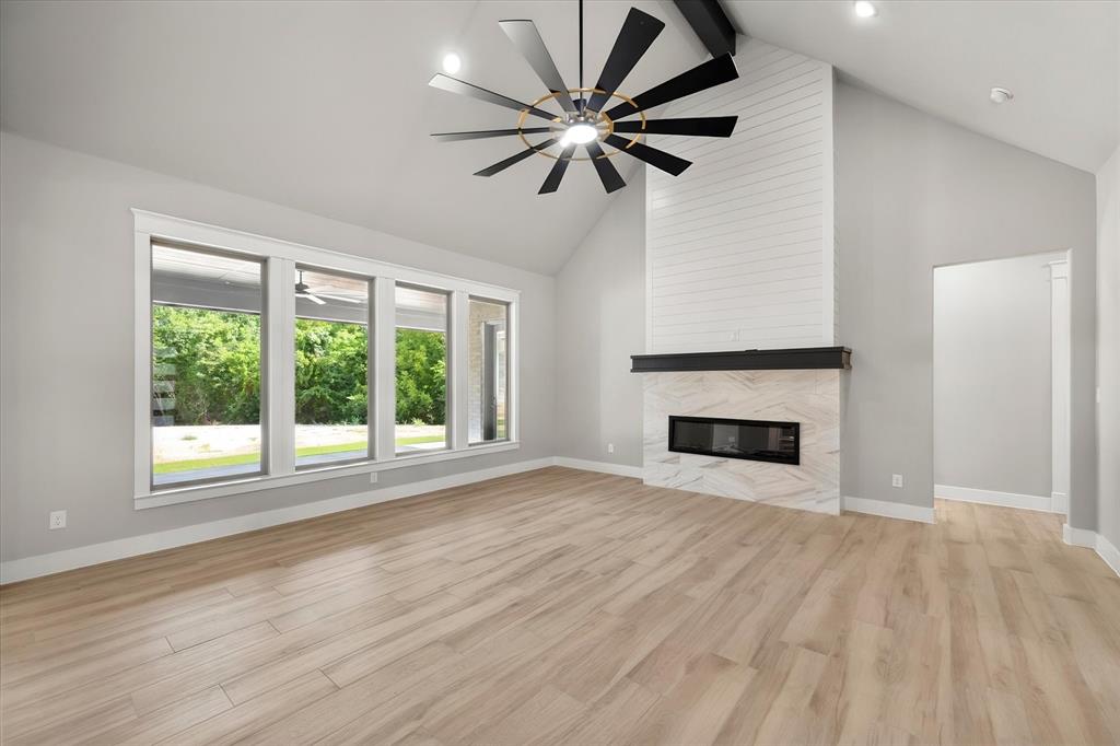 7631 Woodstream Road Midlothian, TX 76065 - Photo 11 of 40 Vaulted ceiling with exposed beam, large picture windows, wood-finish flooring, fireplace with stone surround and shiplap accent, and a contemporary ceiling fan
