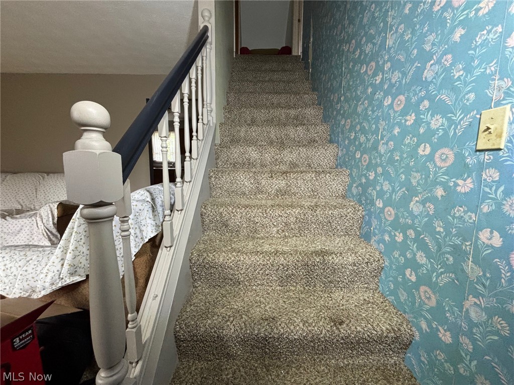 57575 Marietta Road Byesville, OH 43723 - Photo 14 of 25 Carpeted staircase featuring a light gray newel post and balusters, dark gray handrail, and floral wall covering